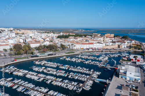 Ria Formosa shows a busy dock filled with boats. Faro's Old Town can be seen in the background on a clear, sunny day in Algarve, Portugal