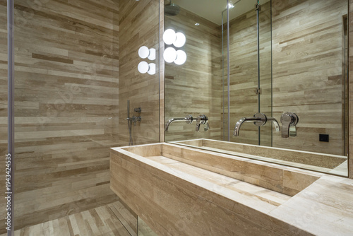 A bathroom shows tiled wooden style walls and a sink area with two faucets. Light fixtures above the mirror provide bright illumination. The setting appears clean and organized