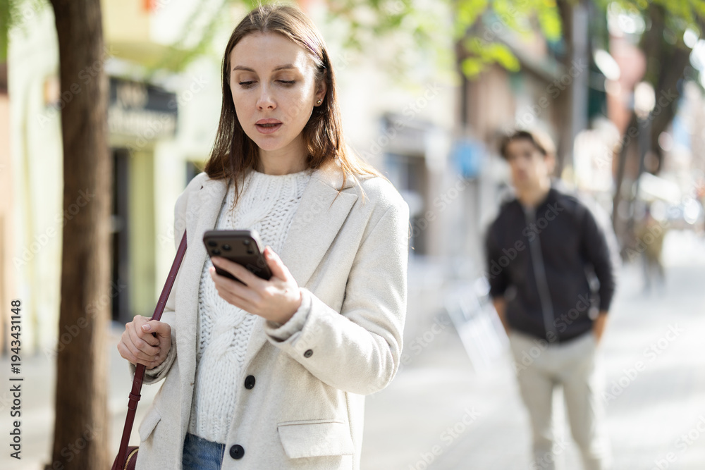 Fototapeta premium Portrait of woman with mobile phone walking along the street of a spring city