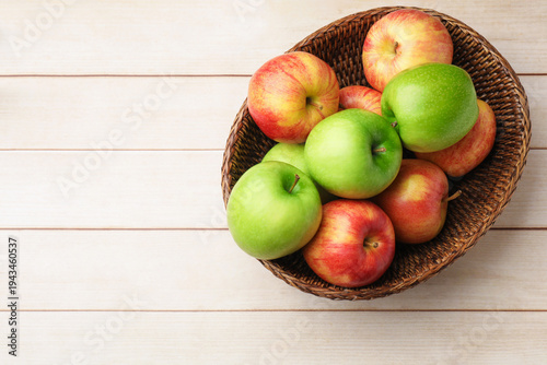 Fresh ripe red and green apples in wicker bowl on light wooden table, top view. Space for text