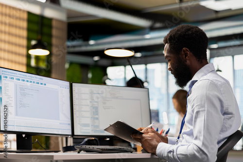 Photos Programmer reviews documentation while coding on PC in modern office
