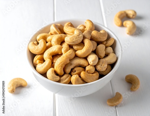 A bowl of toasted cashews with stray nuts on a white, textured surface