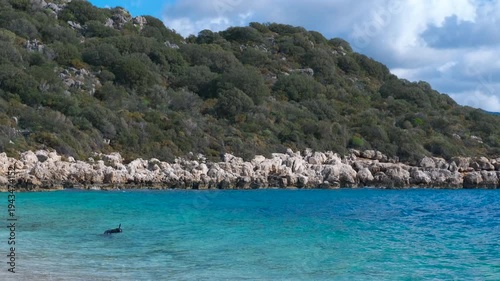 Scuba diver emerging from turquoise water near rocky coast. Crystal-clear turquoise water gently laps against a rocky coastline as a scuba diver surfaces