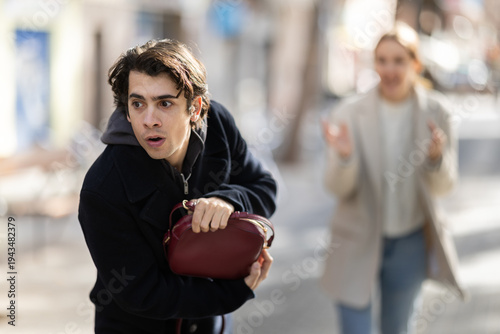 Tablou pe pânză Male thief attempts to steal woman's handbag from frightened young woman