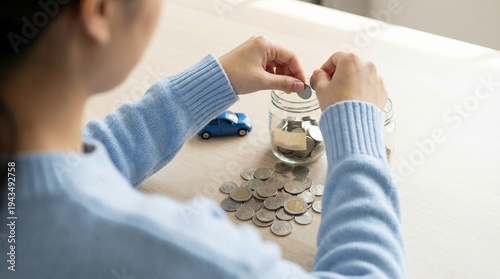 Hands stacking coins beside a miniature blue toy car for saving concept