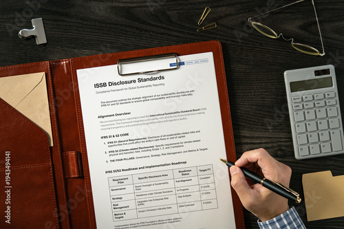 ISSB Disclosure Standards: Realistic mock-up mock placed on  with calculator, pen, sticky note. Contributor-created fictional business document for illustrative purposes.