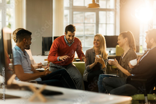 Coworkers laughing during coffee break in modern office