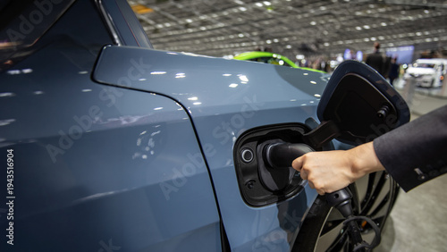 Photography Close-up of a businessman plugging an electric vehicle charging cable into a black EV at a charging station, symbolizing clean energy and electric mobility