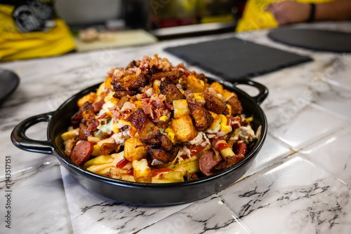 Delicious loaded fries with melted cheese, bacon, and herbs served on a black stone plate in a restaurant.