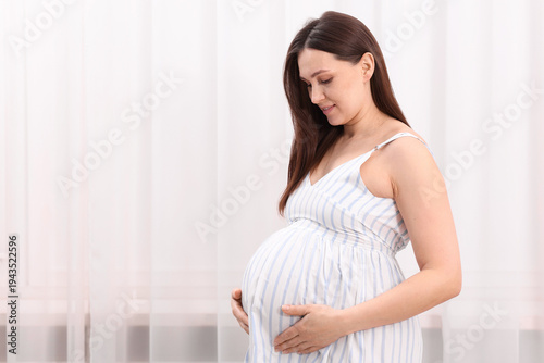 Beautiful pregnant woman touching her belly near curtains at home, space for text Free Download Beautiful pregnant woman touching her belly near curtains at home, space for text - GFXLoad