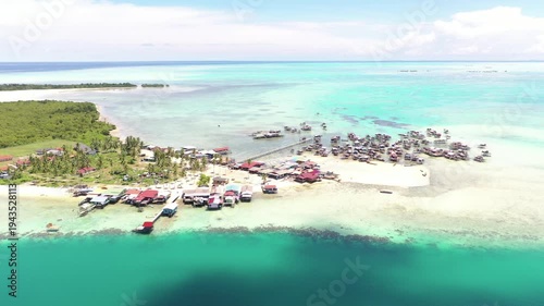 Aerial view of sea village over clear turquoise waters in Omadal Island Semporna, Sabah, Malaysia. Scenic seascape with coral reefs, coastal village, and blue tropical sky.