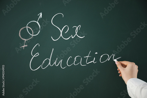 фотографія Woman writing words Sex Education on green chalkboard, closeup