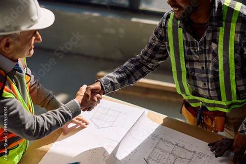 Close up of black worker handshaking with building contractor at construction site.