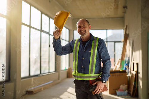 Tableau sur toile Happy mature worker saluting with safety helmet at constriction site and looking at camera