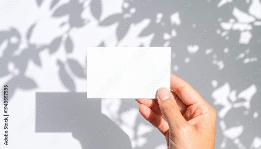 Obraz premium Hand holding blank white business card mockup with bright sunlight leaf shadows