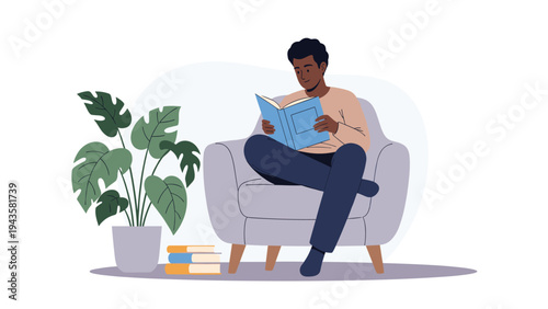 Man sits relaxed in a large grey armchair reading a blue book in a quiet living room corner filled with green indoor plants.
