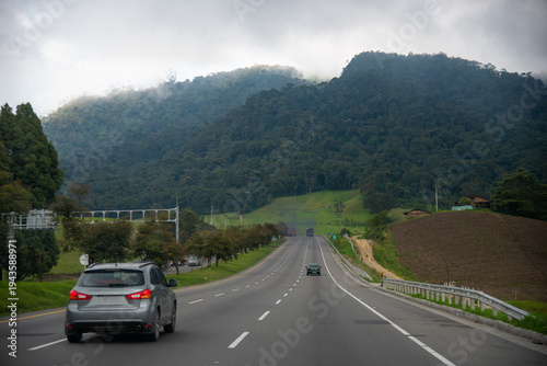 On a cloudy day, several cars drive along a new road in the Colombian countryside.