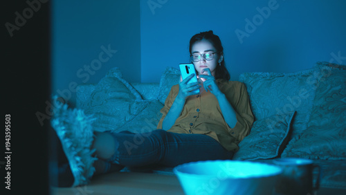 Obraz na plátně Young woman using smartphone on couch in blue ambient light, have fun and enjoy