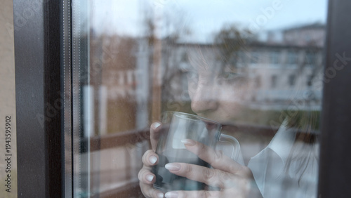 Pensive woman drinking coffee and looking through window reflect, a woman looks thoughtfully out the window
