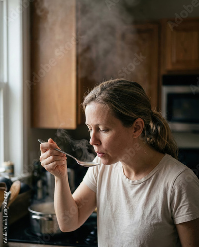 Woman Smelling Steam from Stainless Steel Spoon over Cooking Pot