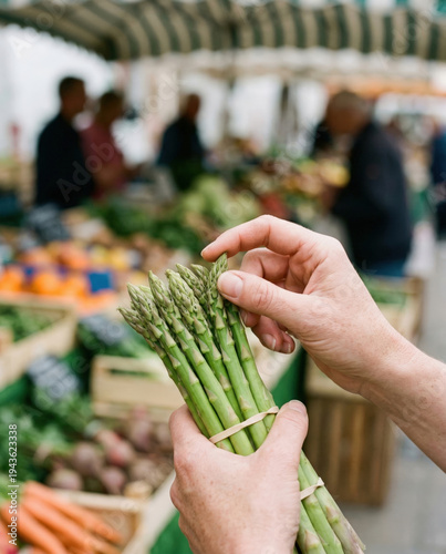 Hands Holding Green Asparagus Spears at Market Stall with Crates