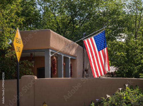 American flag of the U.S.A. on an Adobe style home in Santa Fe New Mexico with a sign saying Dead End green leaves on trees behind horizontal patriarchal political tourism or travel backdrop backgroun