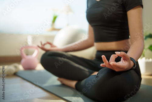 Close up of serene woman meditating in lotus position in a bright room. Wellness and mindfulness concept.