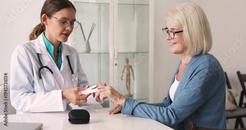 Female doctor placing fingertip pulse oximeter onto woman patient finger, to measure blood oxygen saturation, checking heart rate during medical consultation in clinic office. Health care services