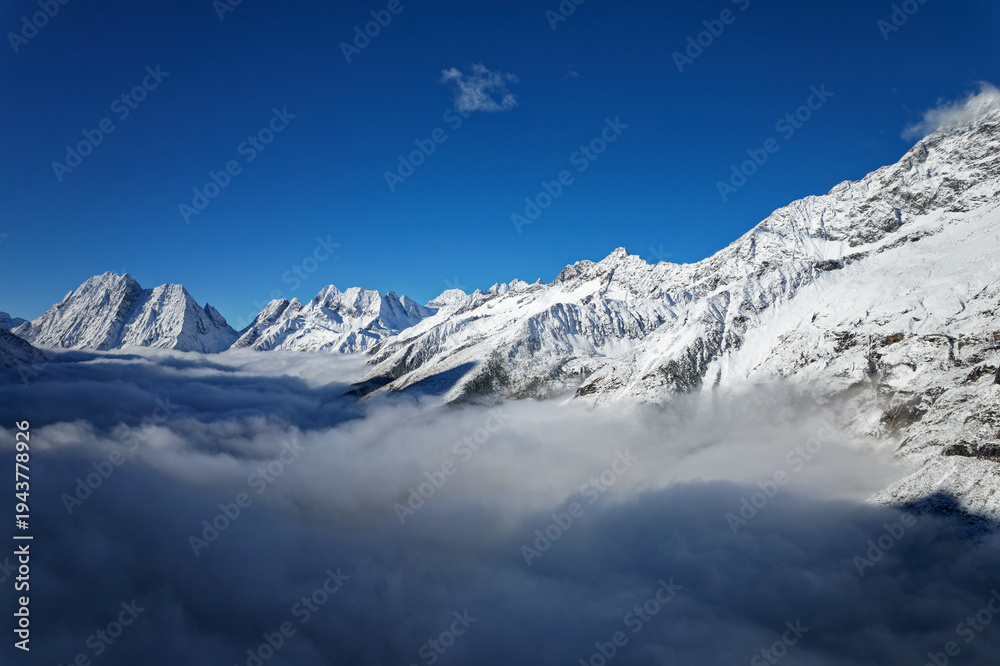 Obraz premium Drone view landscape of Shuangqiao Valley (Shuangqiaogou or Double Bridge Valley) in Mount Siguniang in Sichuan, China. Beautiful snow capped mountains over white clouds in sunny day.