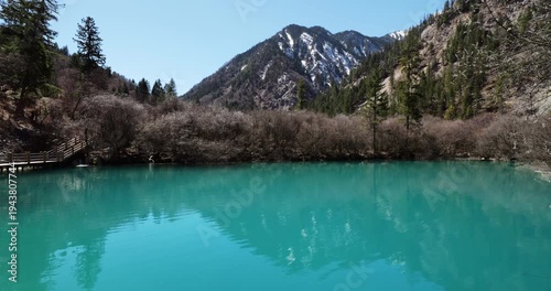 Stunning natural landscape of vibrant turquoise lake with and mountains with slight amount of snow on slopes at background. Rare view of popular Jiuzhaigou Valley without people visible