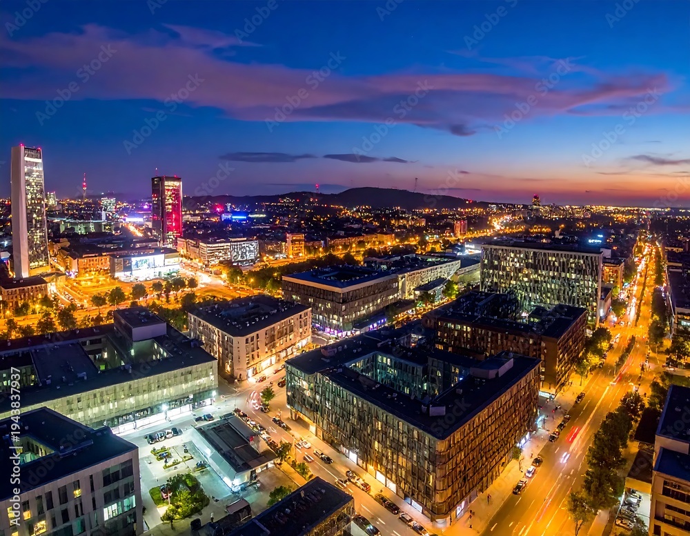 Fototapeta premium Aerial cityscape at dusk with illuminated buildings and streets