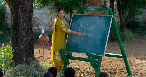 Photography Indian young adult gen z female lady talk speak teach to villager child day under tree rural area