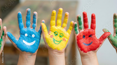Children's hands with colorful painted smiley faces raised upwards