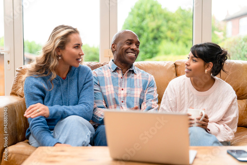 Three friends sit on a sofa in a living room
