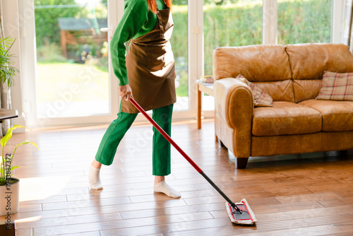 Person cleaning wooden floor in living room during daytime with sunlight coming in from window