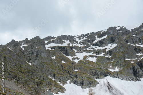Minimal gloomy alpine landscape with sharp rocky ridge with snows in rainy we...
