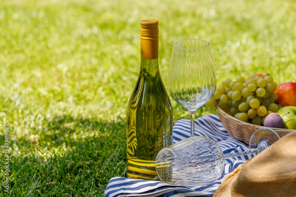 Fototapeta premium Picnic with wine, fruits, and baguette on a green meadow