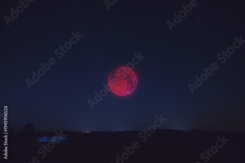 Lunar eclipse, stars and planets above landscape silhouettes.