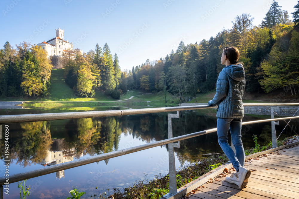Fototapeta premium Girl enjoys аmazing autumn view of old castle and lake of Trakoscan in Zagorje, northern Croatia.