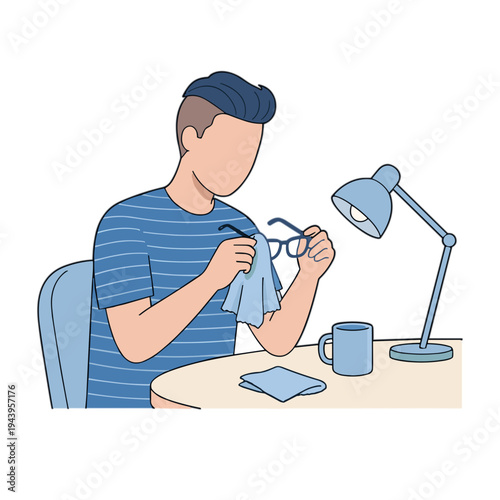 Man sitting at desk cleaning glasses under lamp with mug and phone nearby