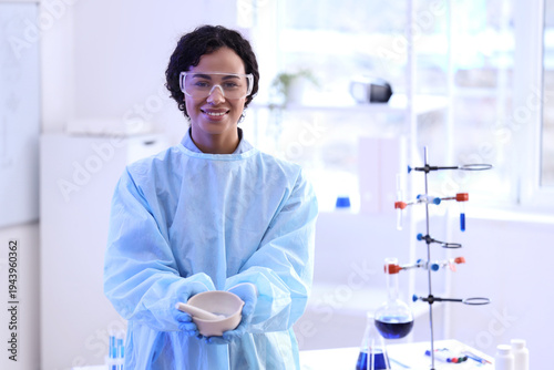 Happy young African-American female chemist with mortar and pestle in lab
