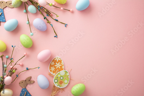 Pastel Easter eggs, spring branches and wooden bunny on pink background with copy space.