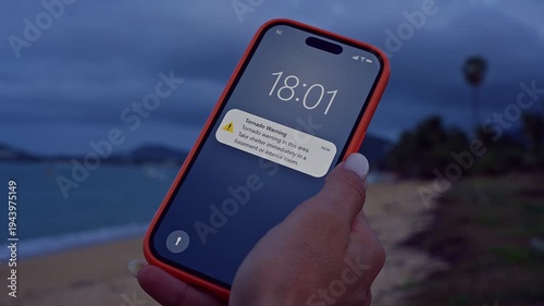 Woman Checking Smartphone With Tornado Warning Notification While Standing on Windy Beach Under Dark Storm Clouds Zoom Shot