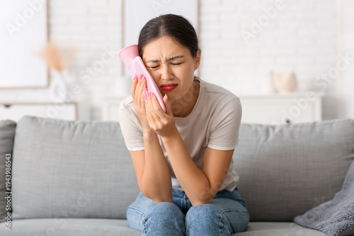 Photography Young Asian woman with hot water bottle suffering from tooth ache on sofa in liv