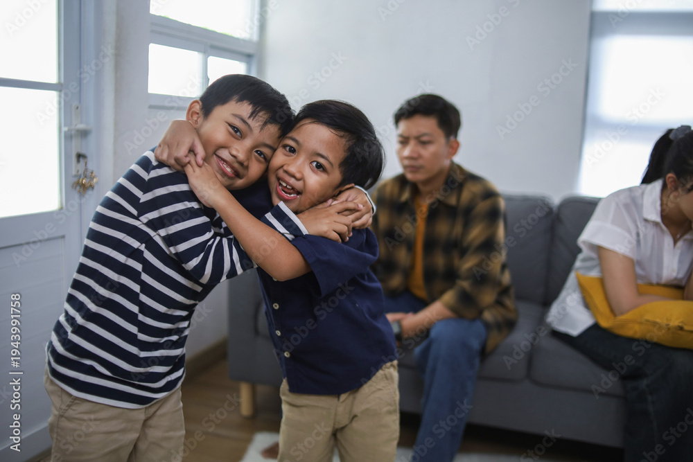 Obraz premium Two Happy Boys Hugging and Smiling in Cozy Living Room While Their Parents Arguing in Background