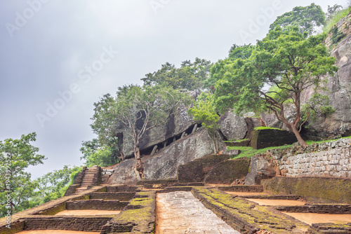 Sigiriya ancient rock fortress in Sri Lanka. Ancient Rock Fortress Foundations and Lush Green Trees Under Overcast Sky, Historical Landscape Setting for Travel and Heritage