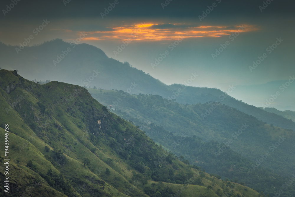 Fototapeta premium Dramatic sunrise Glow Over Lush Green Mountain Peaks and Valleys with Hazy Atmosphere and Vibrant Sky Colors. Mountain landscape near Ella in Sri Lanka.