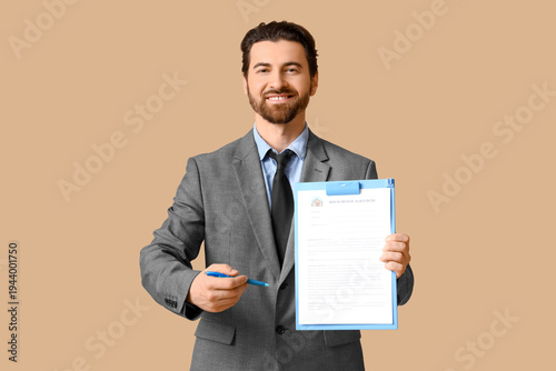 Young happy male real estate agent with house rental agreement and pen on bei...