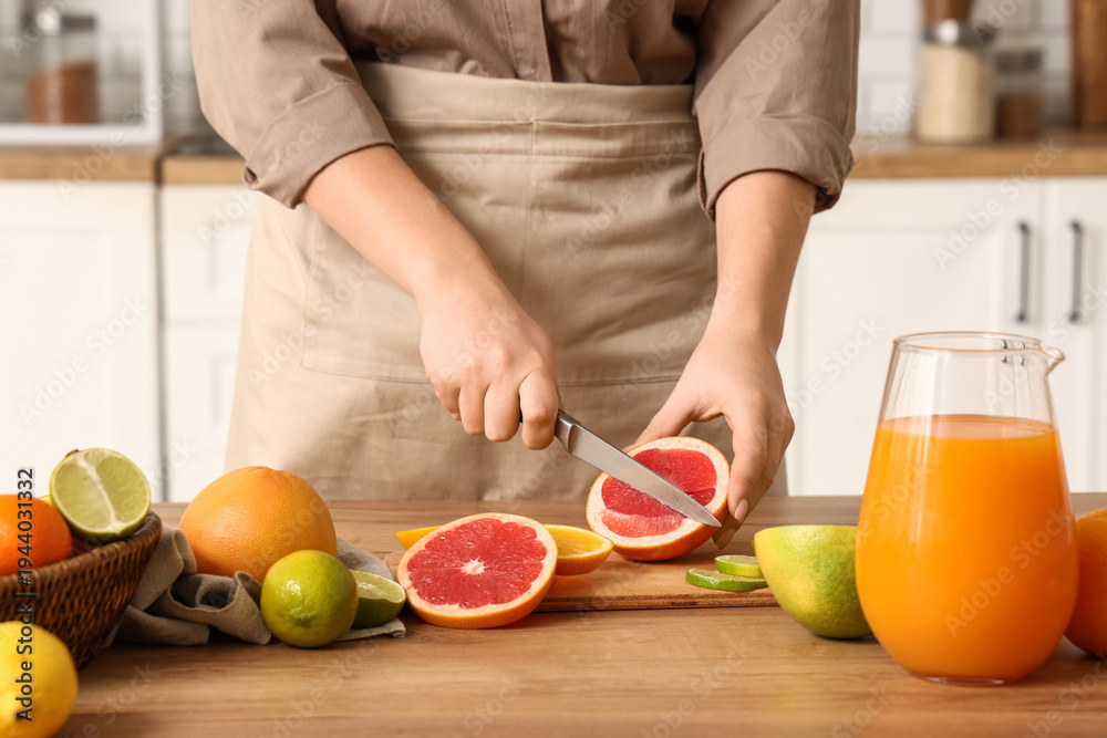 Fototapeta premium Young woman cutting fresh grapefruit on table in kitchen