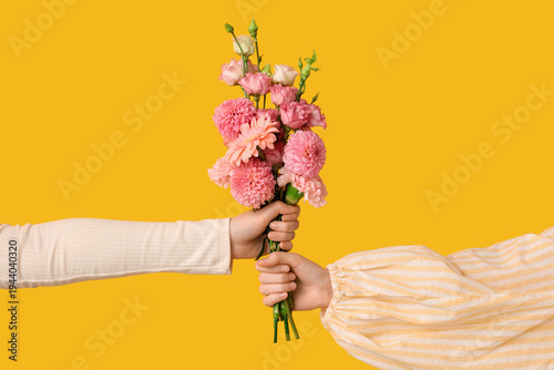 Female hands with beautiful bouquet of flowers on yellow background